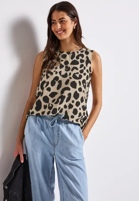 Frau mit ärmellosem Leoparden-Top und heller Jeans lächelt.
